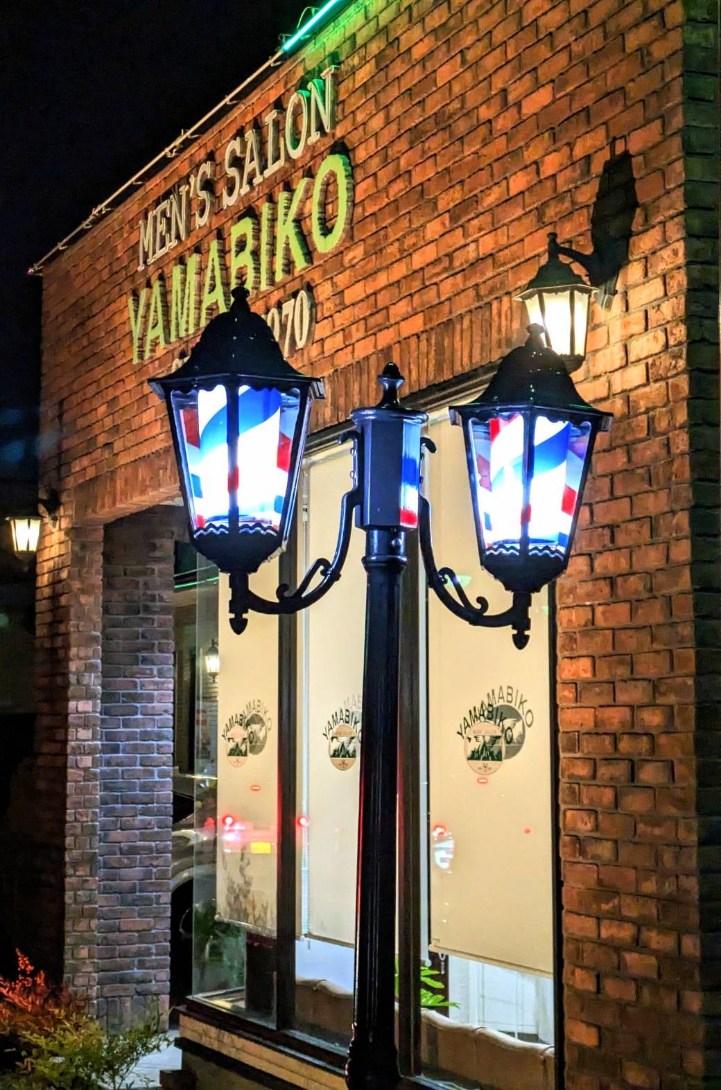 夜に灯りがともるmen's salon YAMABIKOの外観